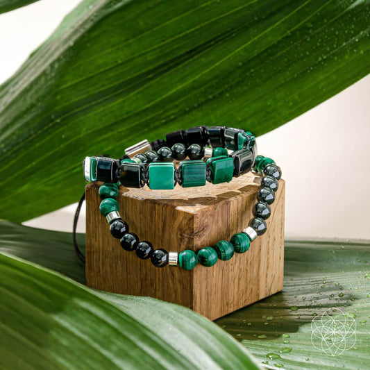 Two beaded bracelets with green and black stones on a wooden display block