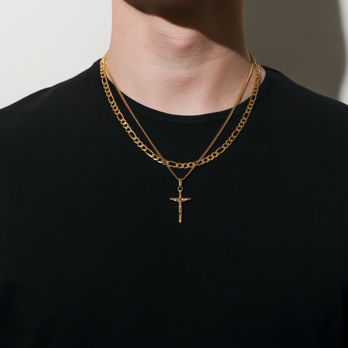 Gold crucifix pendant on figaro chain, worn over black crewneck shirt