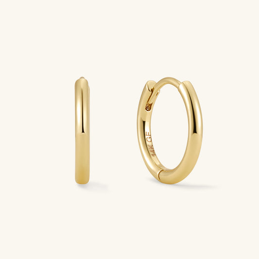 Small gold hoop earrings, hinged clasp visible, pair with smooth round profile.