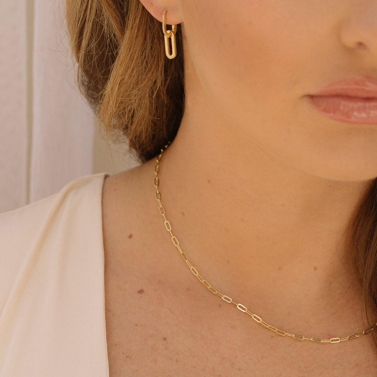 Close-up of gold paperclip chain necklace with oval links and neckline pendant, 2.5 mm