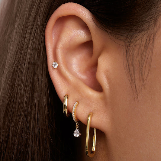 Oval gold hoop earrings on ear, curved hinge and clasp visible