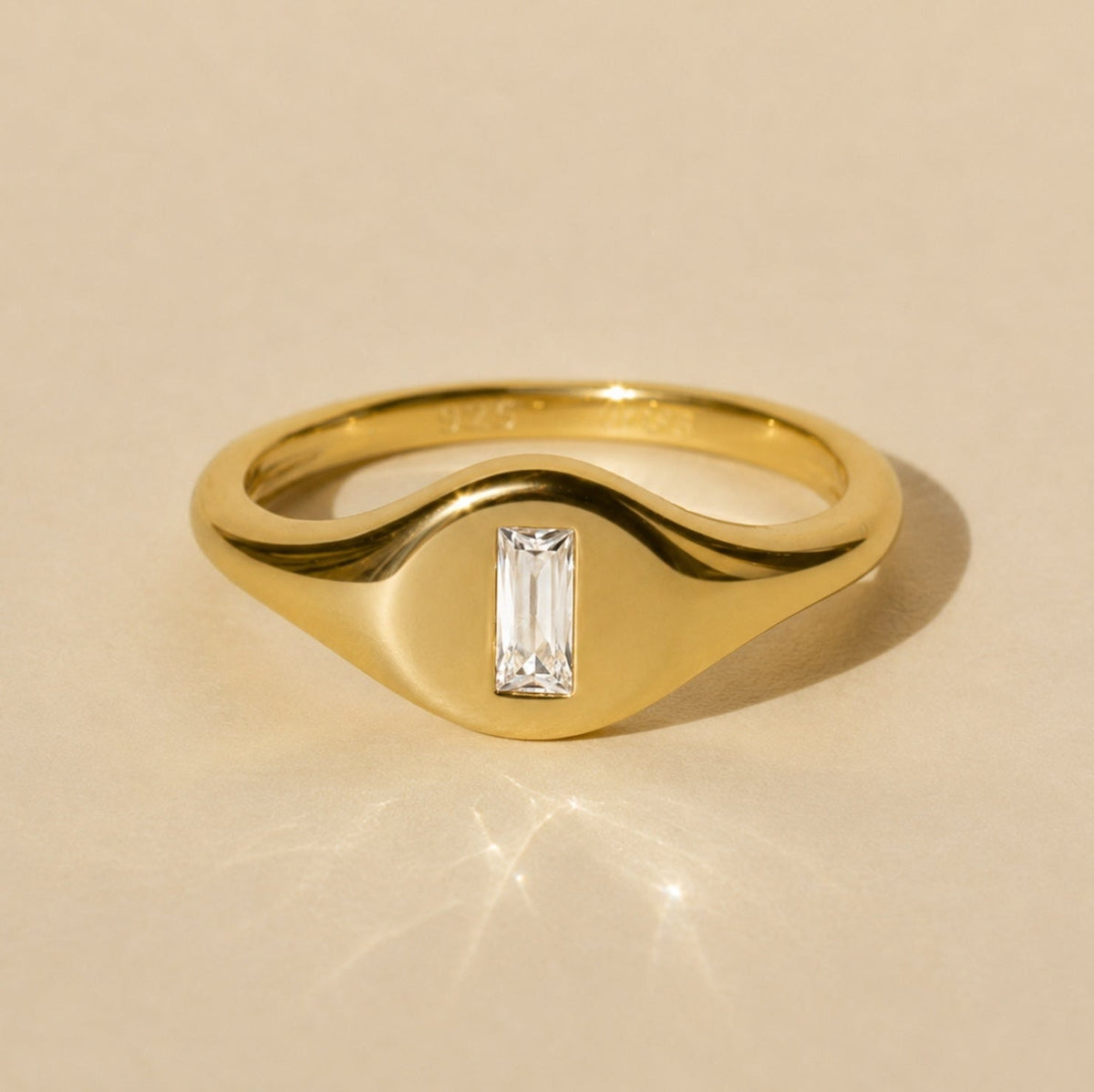 Gold-tone signet ring with baguette-cut crystal center in raised top setting