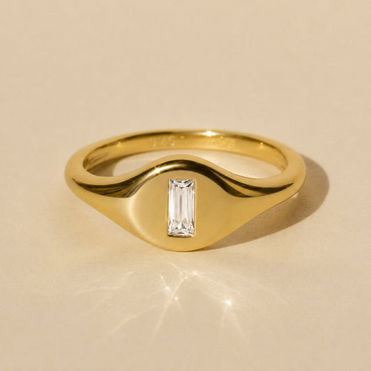 Gold-tone signet ring with baguette-cut crystal center in raised top setting