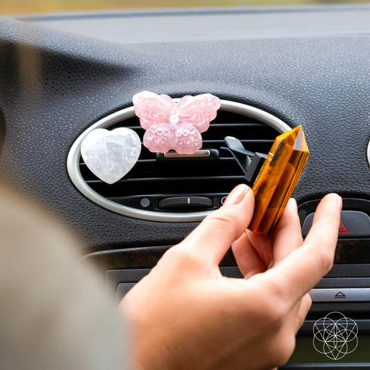 Hand placing crystal pieces on car vent: pink butterfly, white heart, gold point