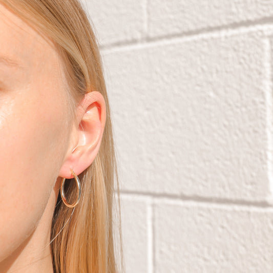 Thin gold-plated hoop earrings on ear, oval 25 mm hoops with hinged clasp