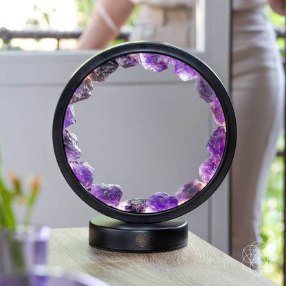 Amethyst crystal halo lamp with purple ring and black base on wooden surface