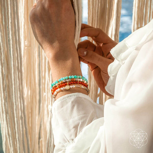Beaded bracelet stack on wrist with turquoise, orange, and white beads and small gold charm.