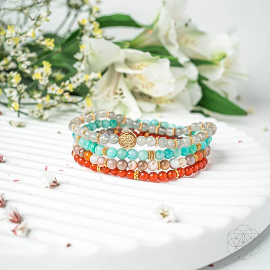 Stack of four beaded bracelets with turquoise, orange, and white stones on a white surface.