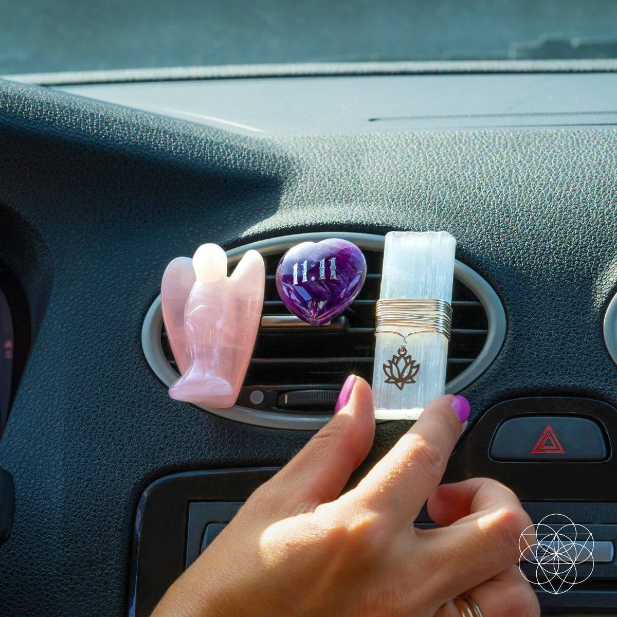 Hand adjusts car vent crystal set with rose quartz angel, amethyst heart, and metal clip