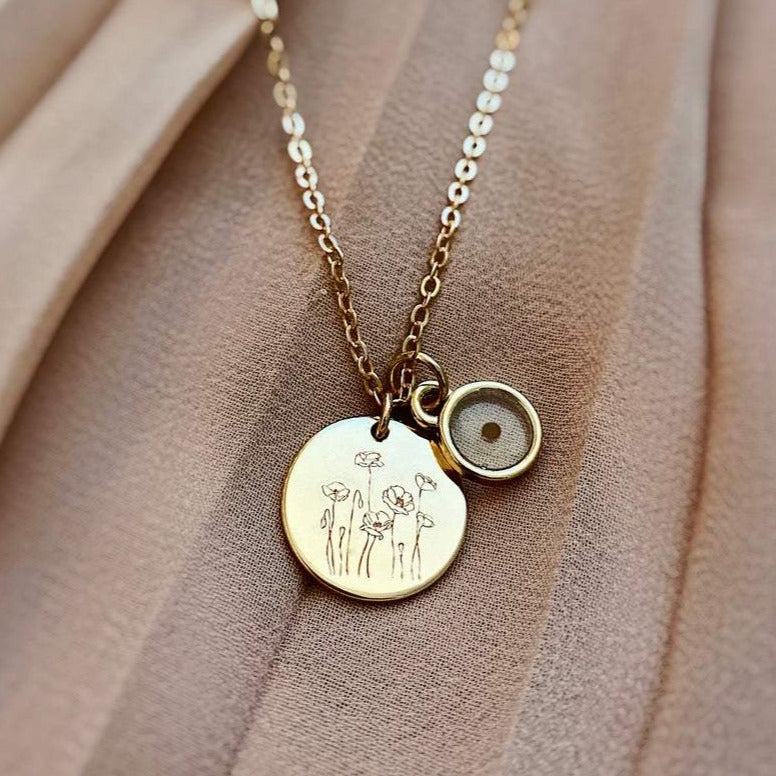 Close-up of engraved poppy pendant and mustard seed charm on a gold-tone chain