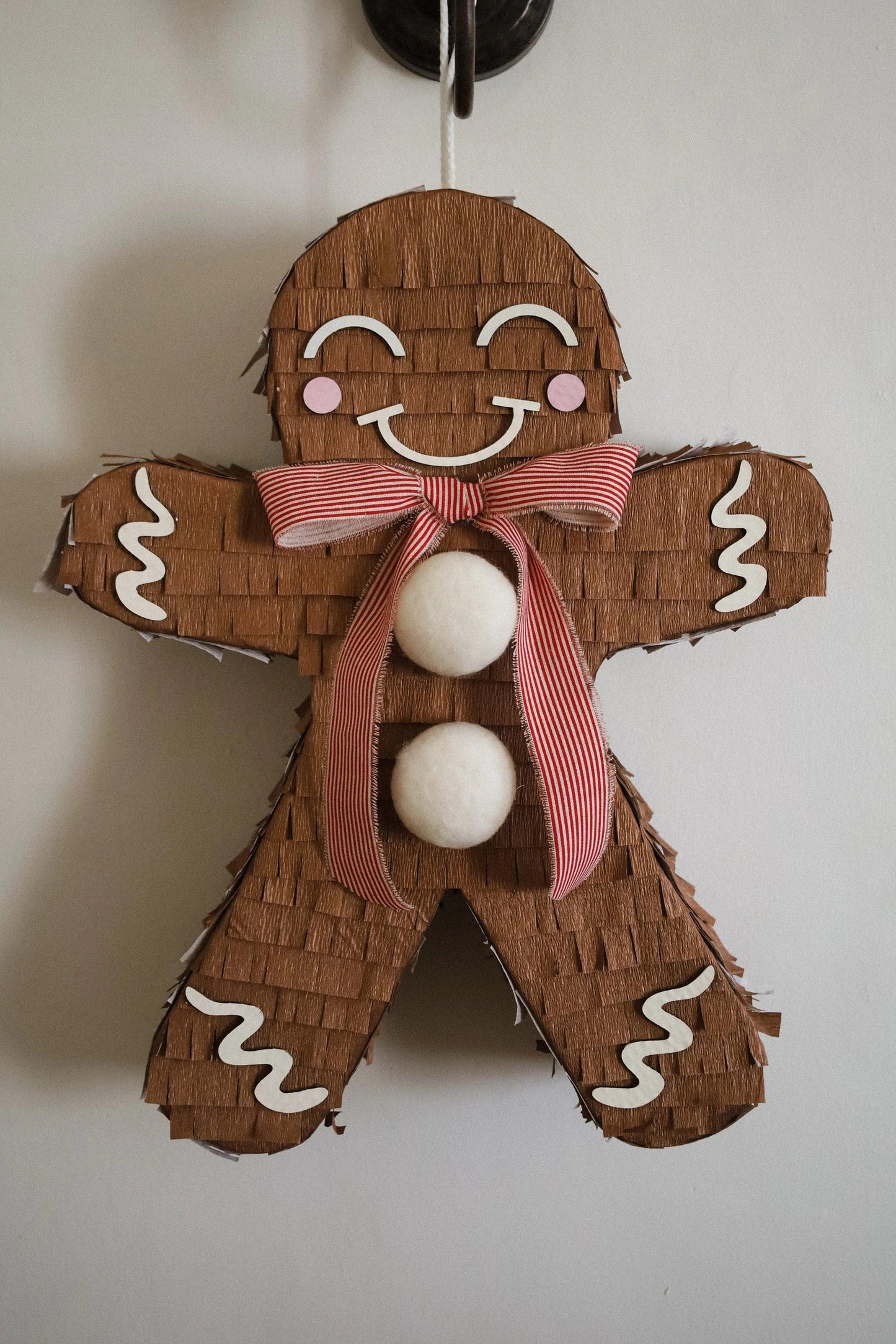 Hanging gingerbread man piñata with smiling face, red striped bow, three white balls