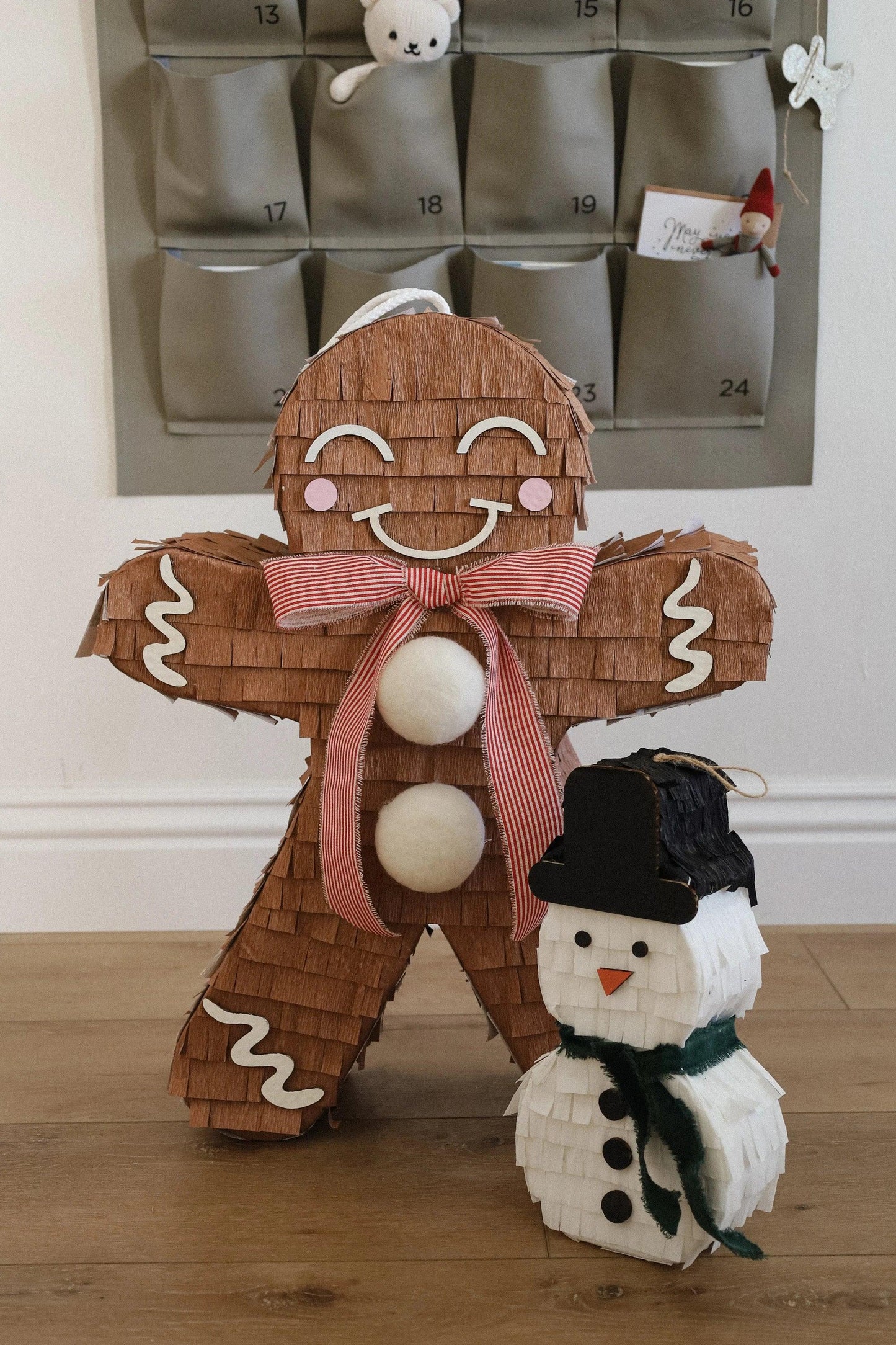 Brown gingerbread man piñata decoration with smiling face, red bow, white pom-poms