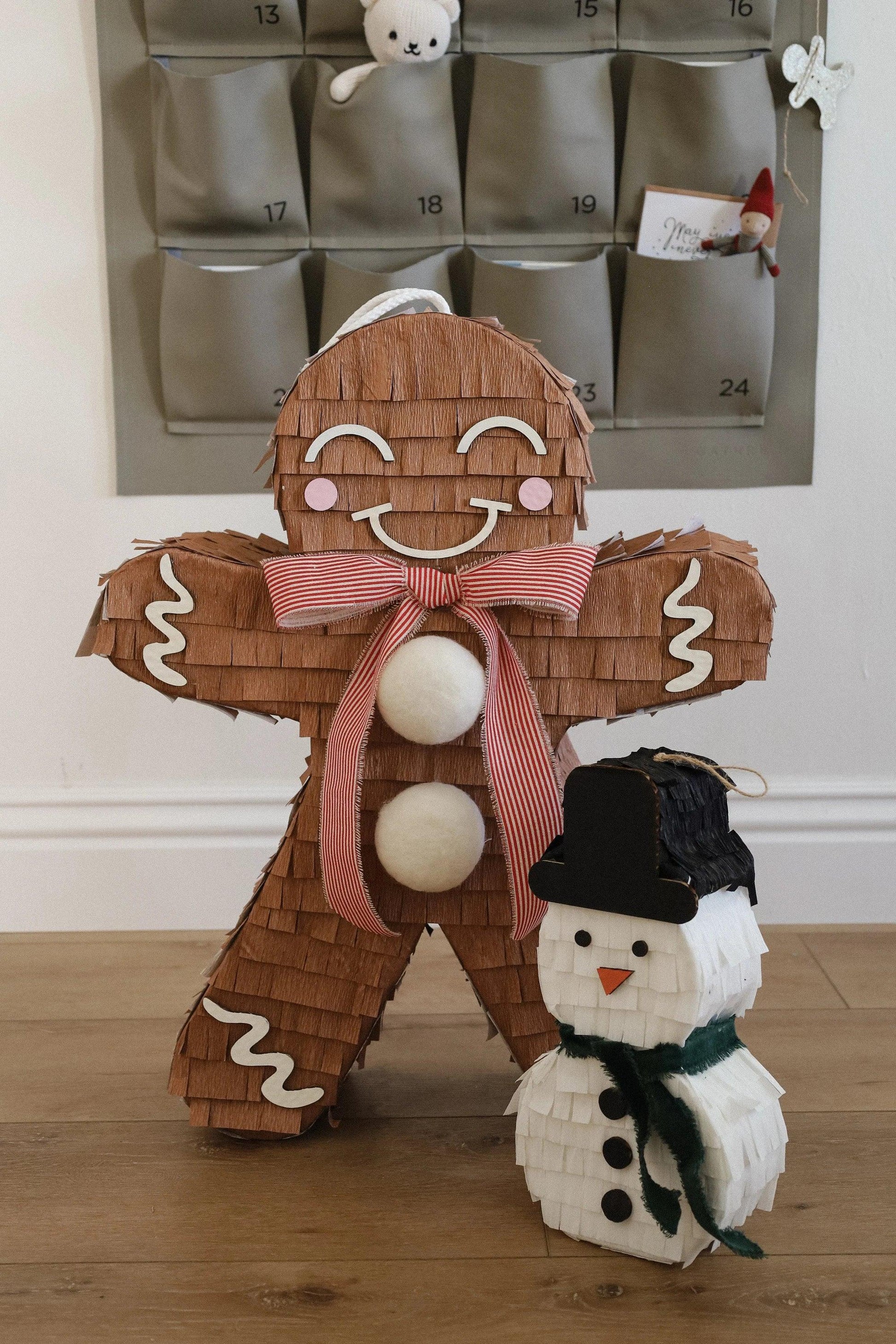 Brown gingerbread man piñata decoration with smiling face, red bow, white pom-poms