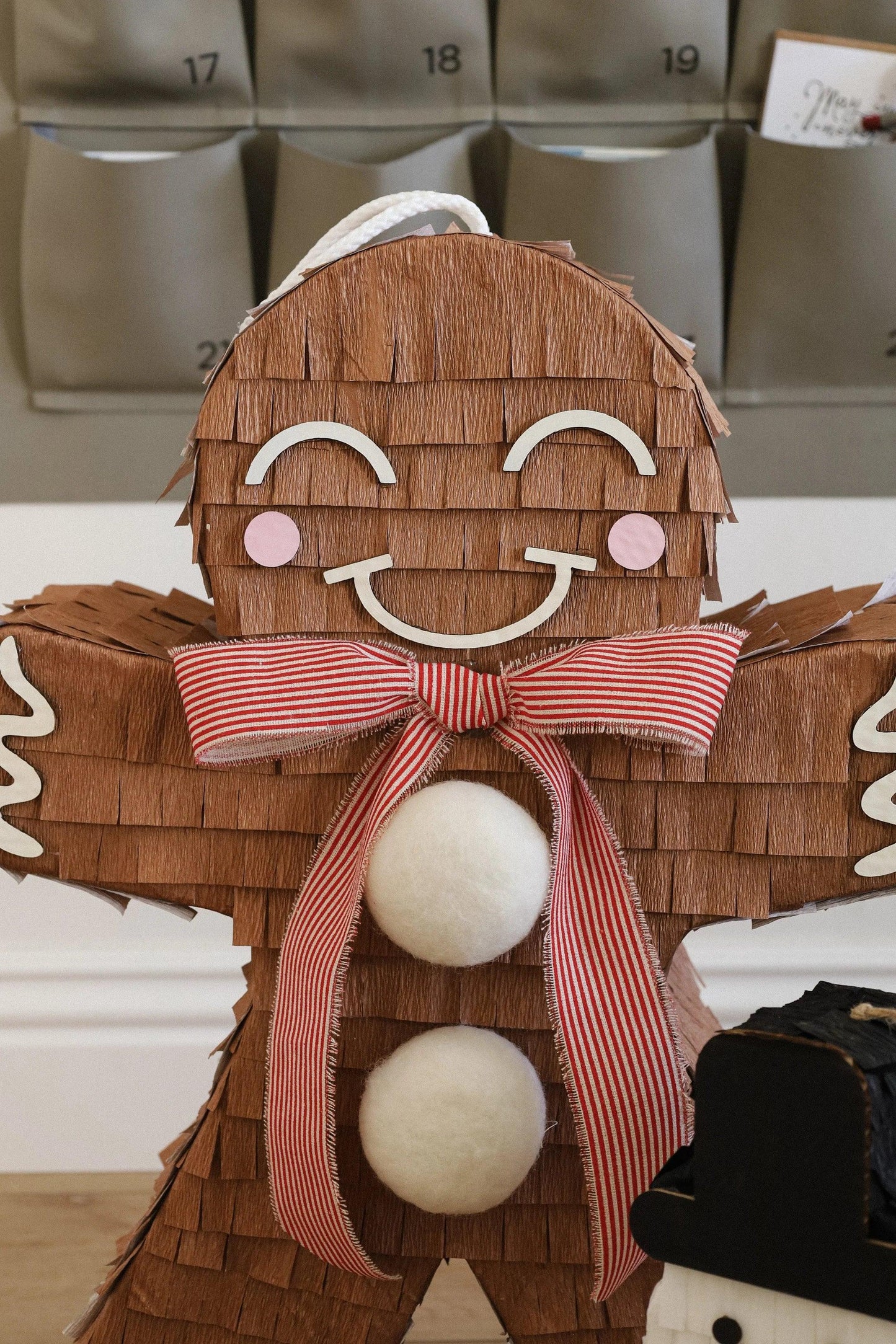 Close-up gingerbread man piñata face and red striped bow with white pom-poms
