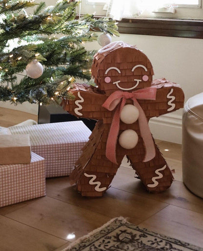 Handmade gingerbread man piñata with red striped bow and three white candy balls