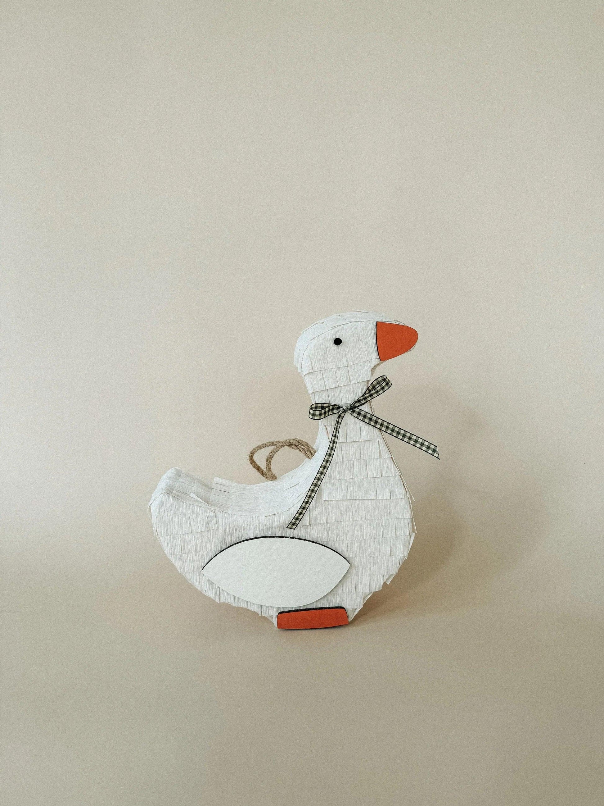 White goose piñata with orange beak, plaid ribbon tie, and hanging loop