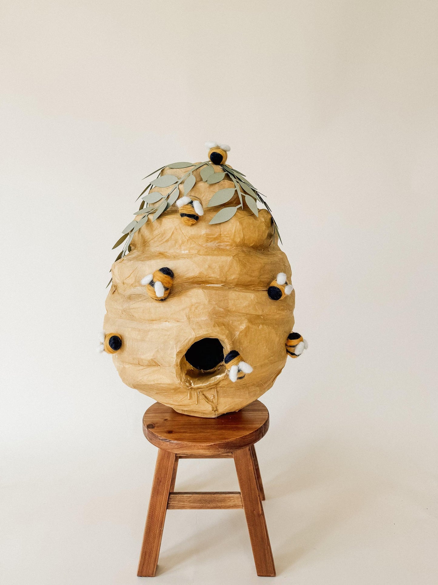 Handmade bee hive piñata with plush bees and leaf top, front view on wooden stand