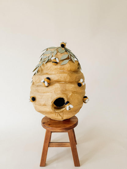 Handmade bee hive piñata with plush bees and leaf top, front view on wooden stand