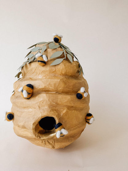 Beehive-shaped piñata with open candy hole and felt bees accents, front view