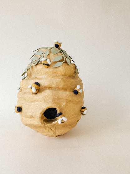 Beehive piñata, tan paper texture with leaf crown and dangling plush bee details
