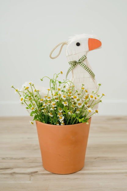 White goose piñata standing in a pot, orange beak and green plaid bow