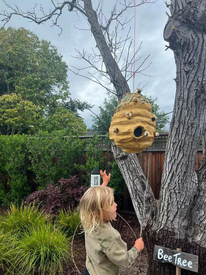 Hanging bee hive piñata with leaf crown and plush bee decorations outdoors