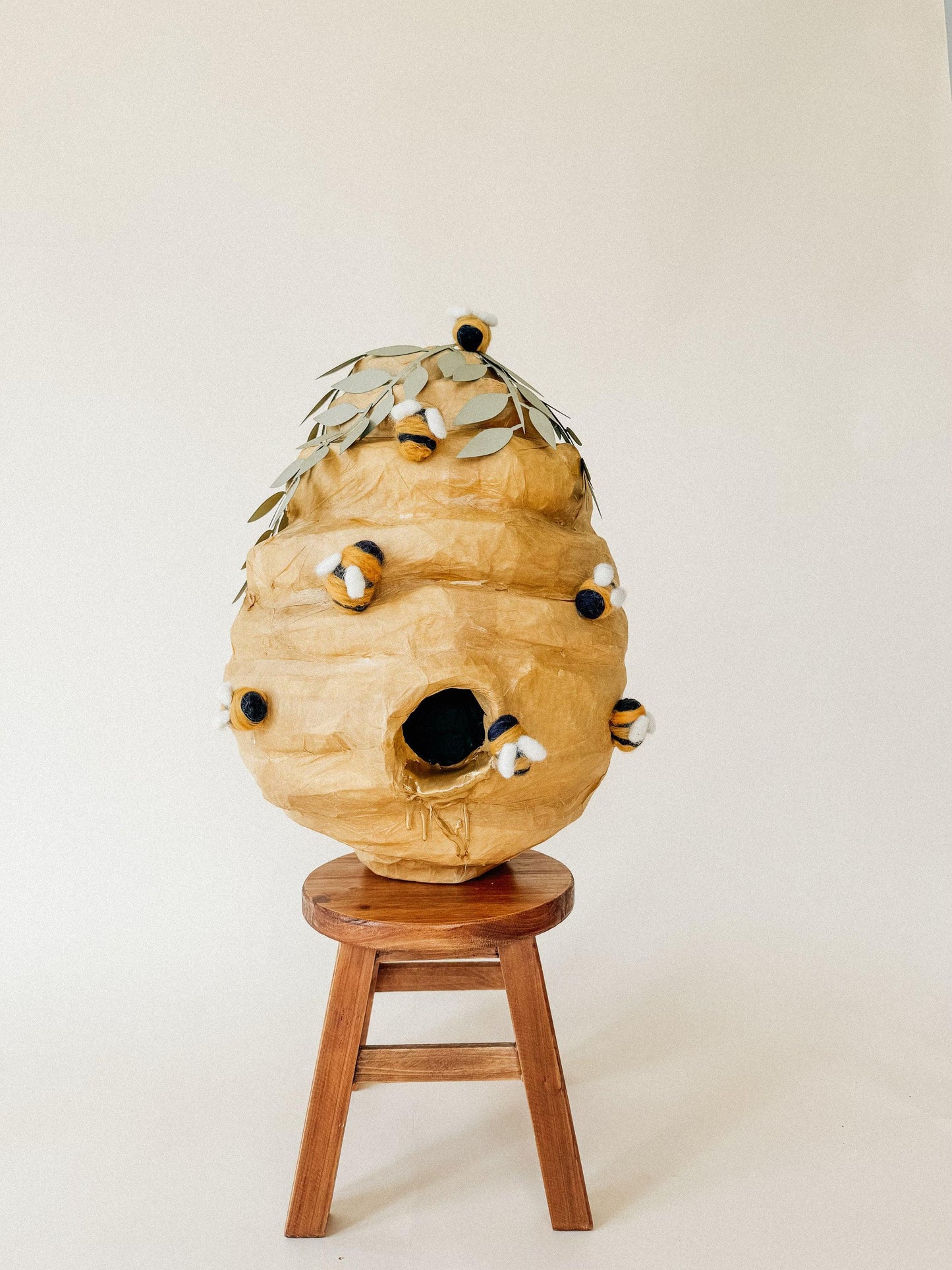 Beehive piñata on wooden stool, leaf crown and felt bees on tan paper surface