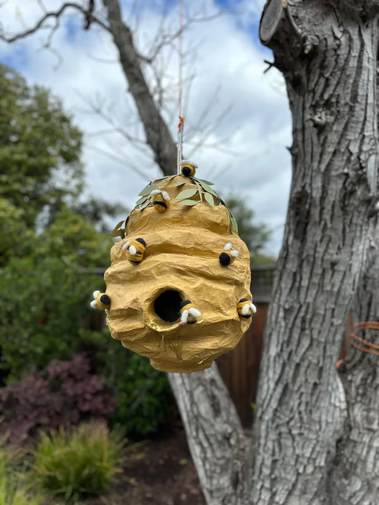 Beehive-shaped piñata hanging from above, leaf top and plush bee details