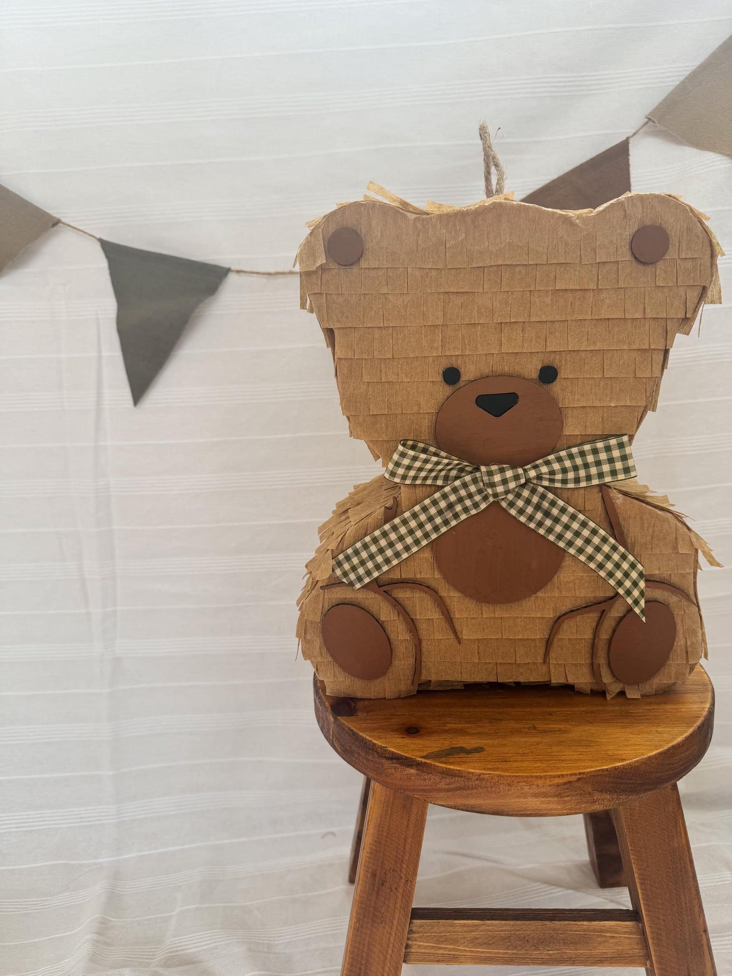 Teddy bear piñata on stool, tan cardboard, checkered bow, paw cutouts