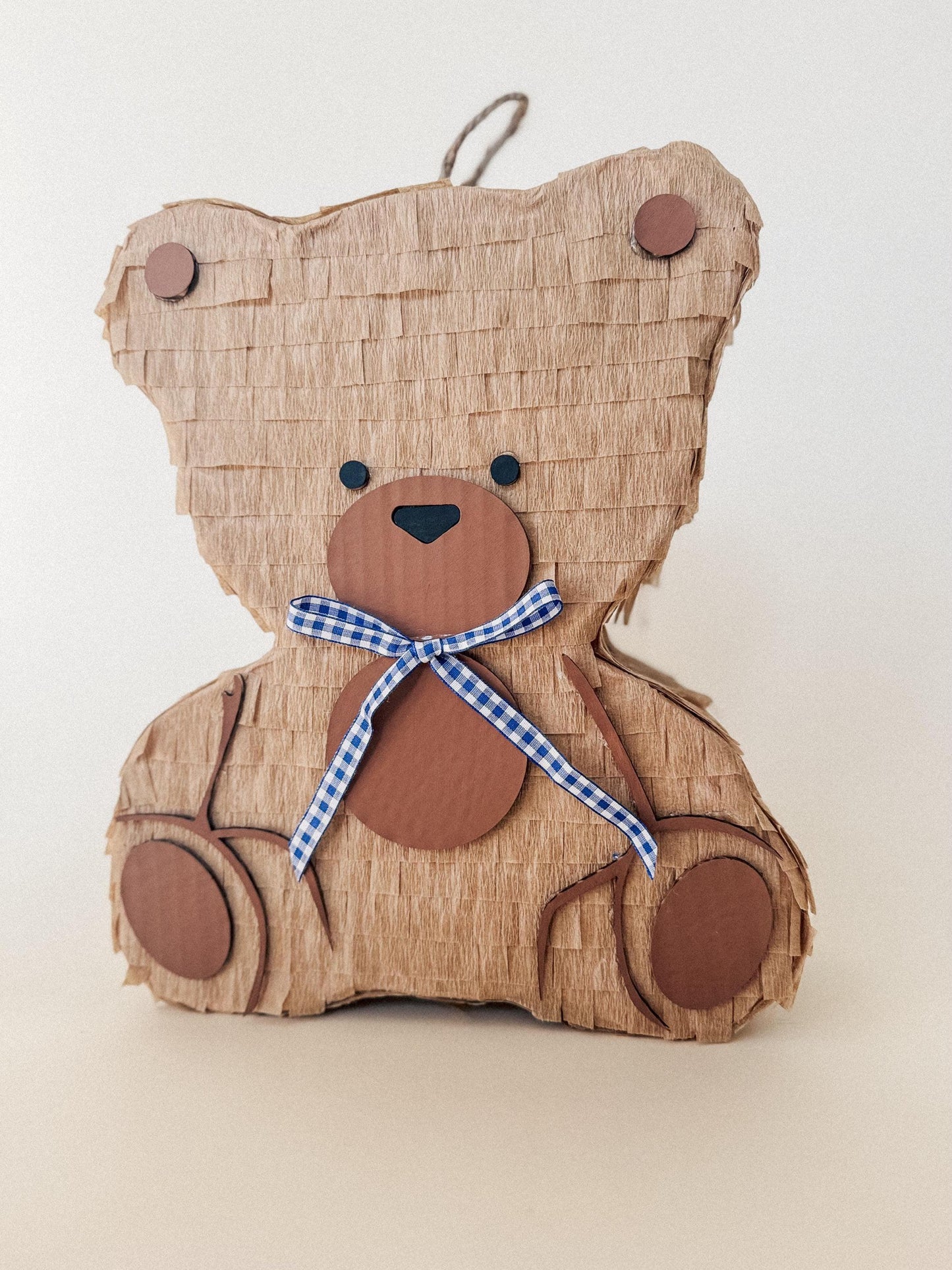 Teddy bear piñata close-up, tan paper, brown nose, blue-and-white checkered bow