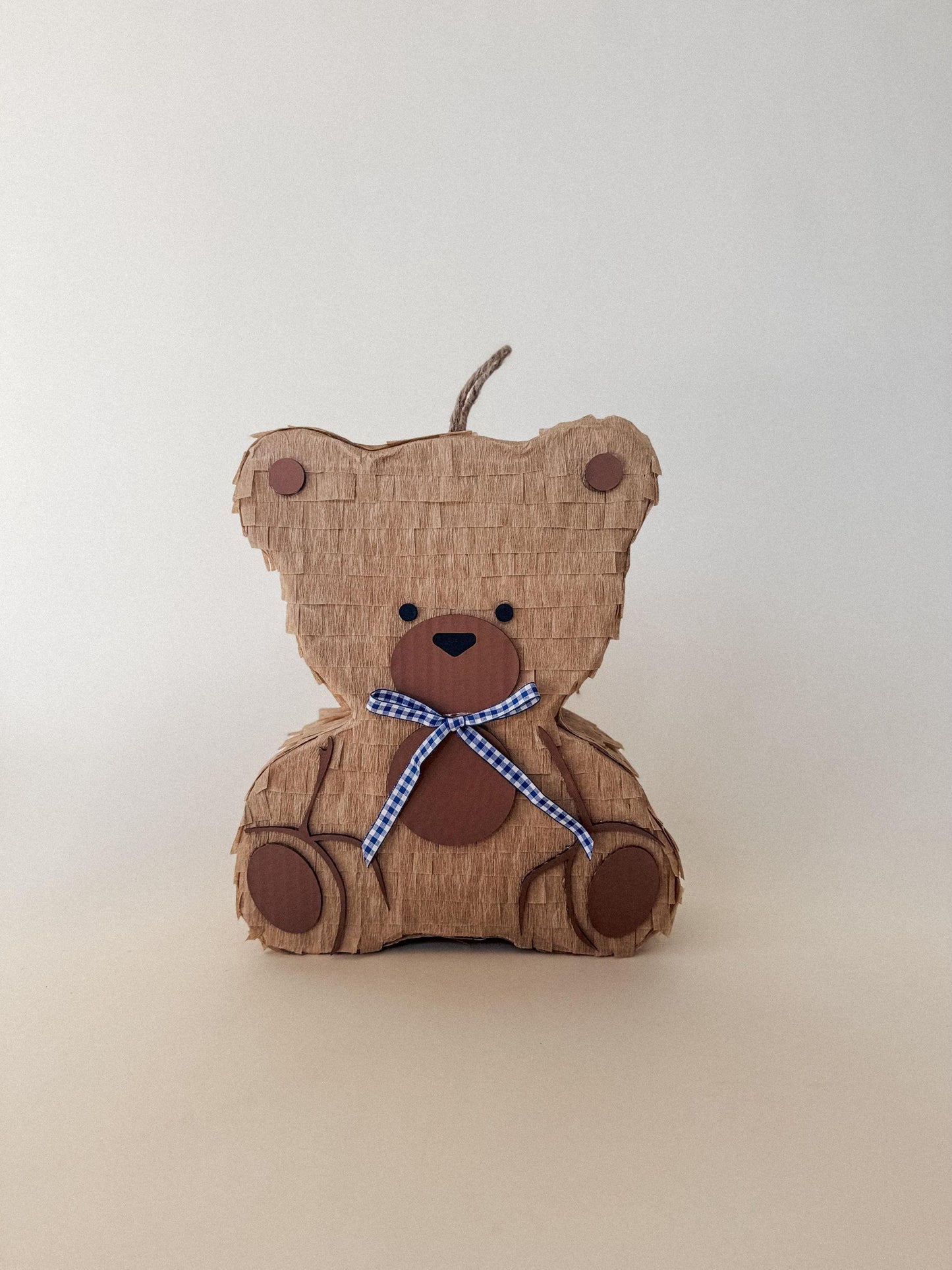 Teddy bear piñata side view, tan layered panels, loop handle, blue checkered neck tie