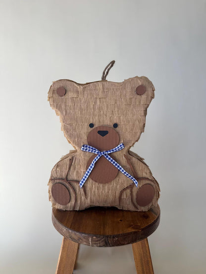 Teddy bear piñata front on round stool, tan cardboard, blue plaid bow, paw details