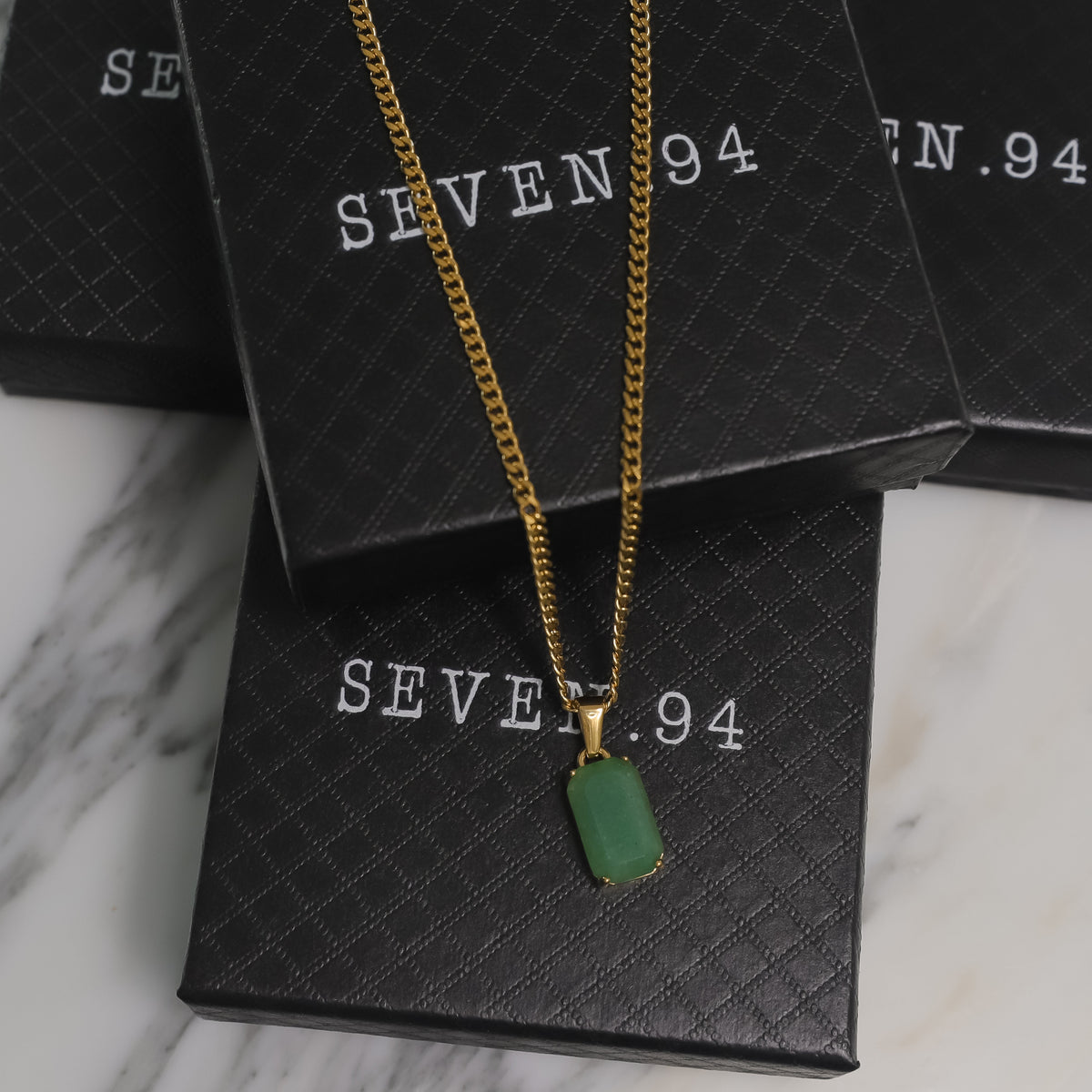 Gold chain necklace with green rectangular stone pendant on a gift bag