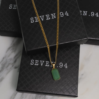 Gold chain necklace with green rectangular stone pendant on a gift bag