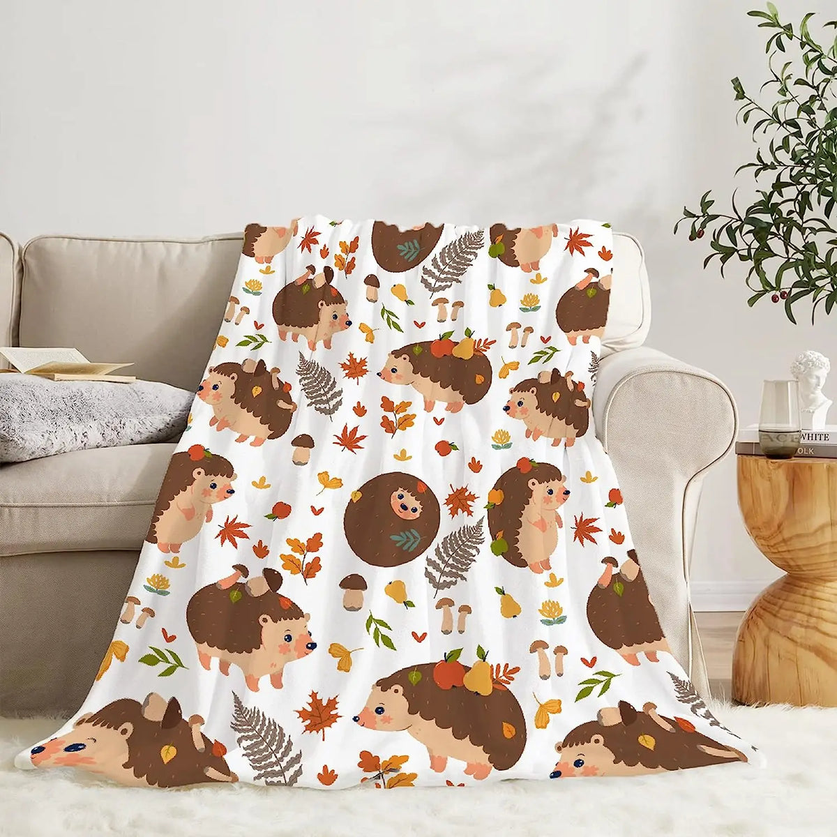 Hedgehog and autumn leaf blanket, white with brown hedgehogs and orange leaves, draped on couch