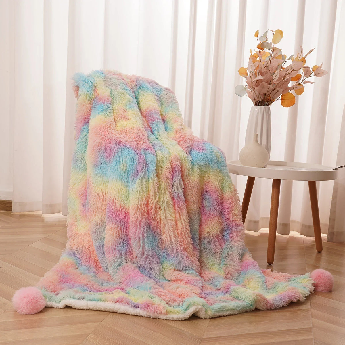 Pastel rainbow fluffy blanket with pom-poms, folded on the floor near a small table