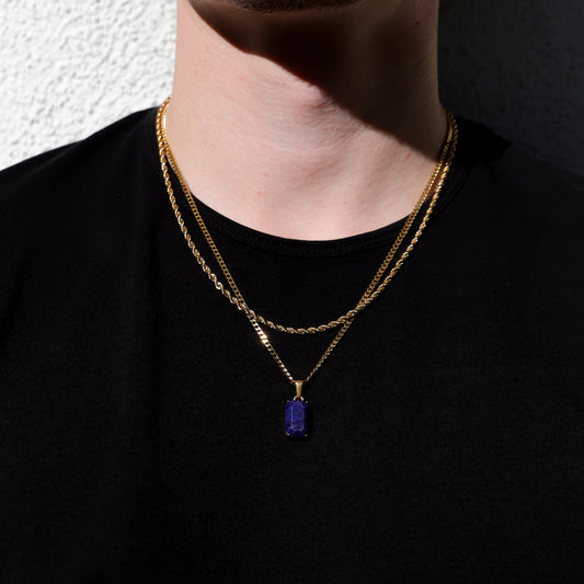 Layered gold-tone chain necklace with blue rectangular pendant, close-up at neckline