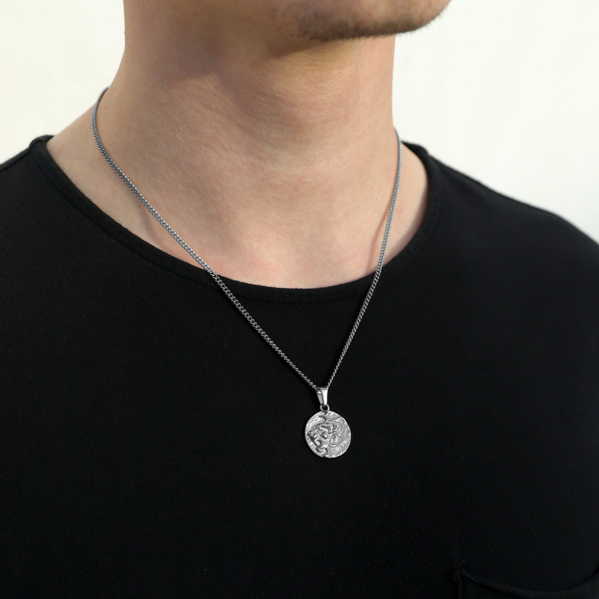 Silver coin pendant necklace with lion face medallion pendant and fine chain, front view.