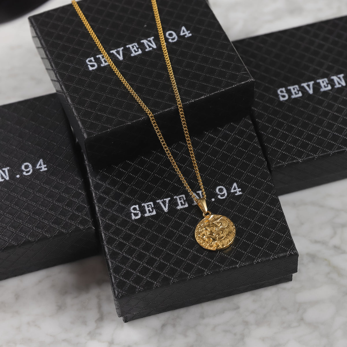 Gold coin pendant necklace resting on SEVEN 9.4 boxes, round lion medallion visible.
