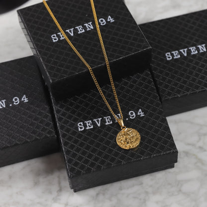 Gold coin pendant necklace resting on SEVEN 9.4 boxes, round lion medallion visible.