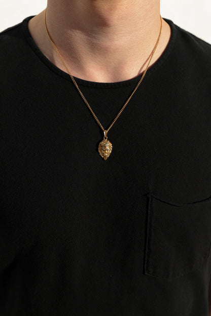 Gold-tone lion head pendant necklace with fine chain, worn over black crew-neck shirt.