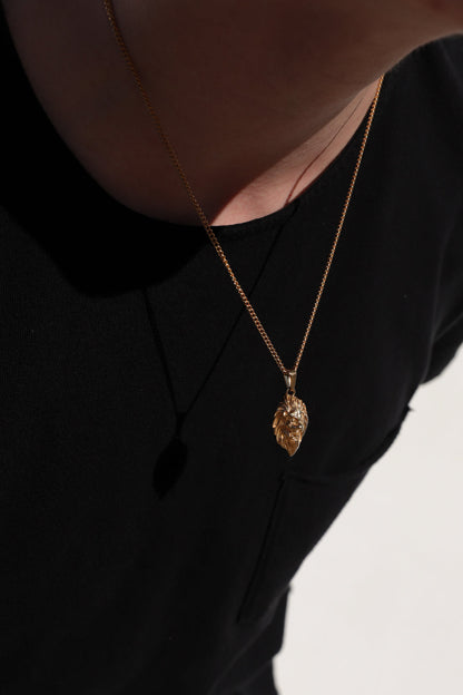 Gold-tone lion head pendant necklace with thin chain, worn at neckline in side view.