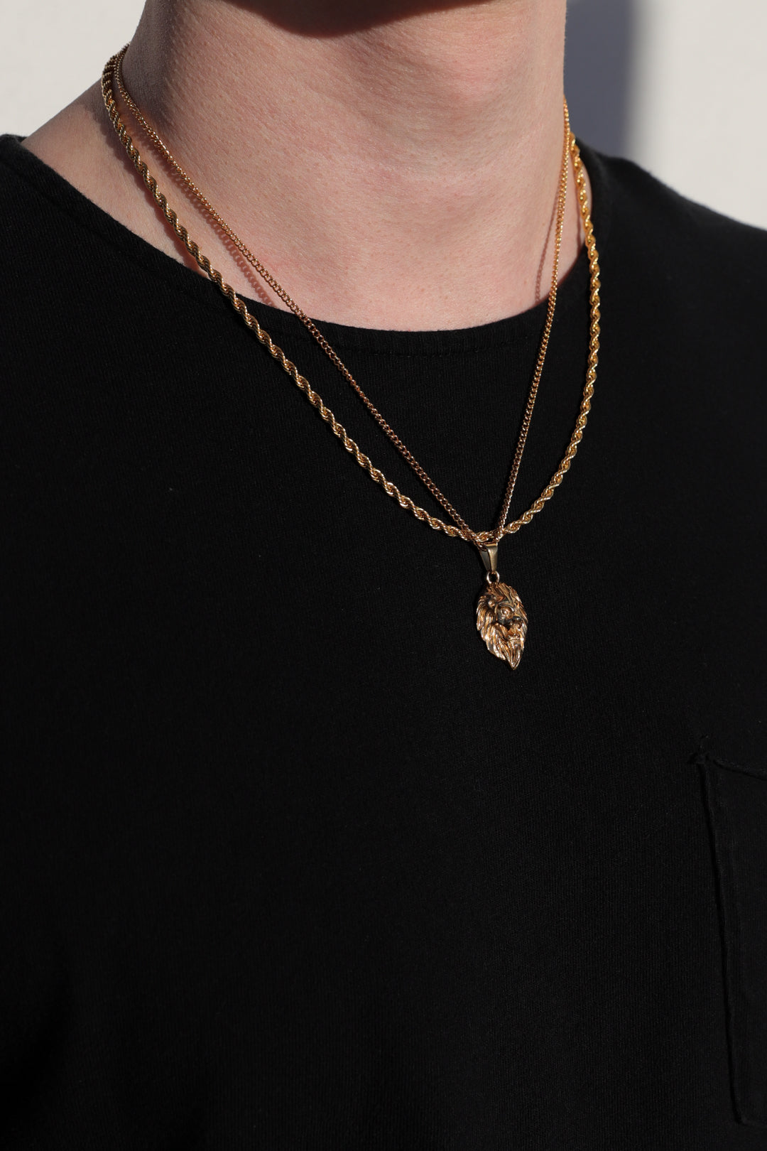Gold-tone lion head pendant necklace on cable chain, layered with another chain at neck.