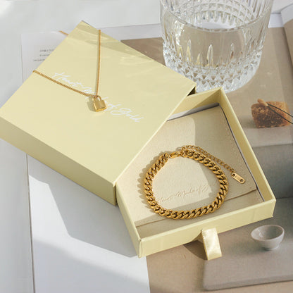 Gold curb chain bracelet resting in a jewelry box, with clasp tag.