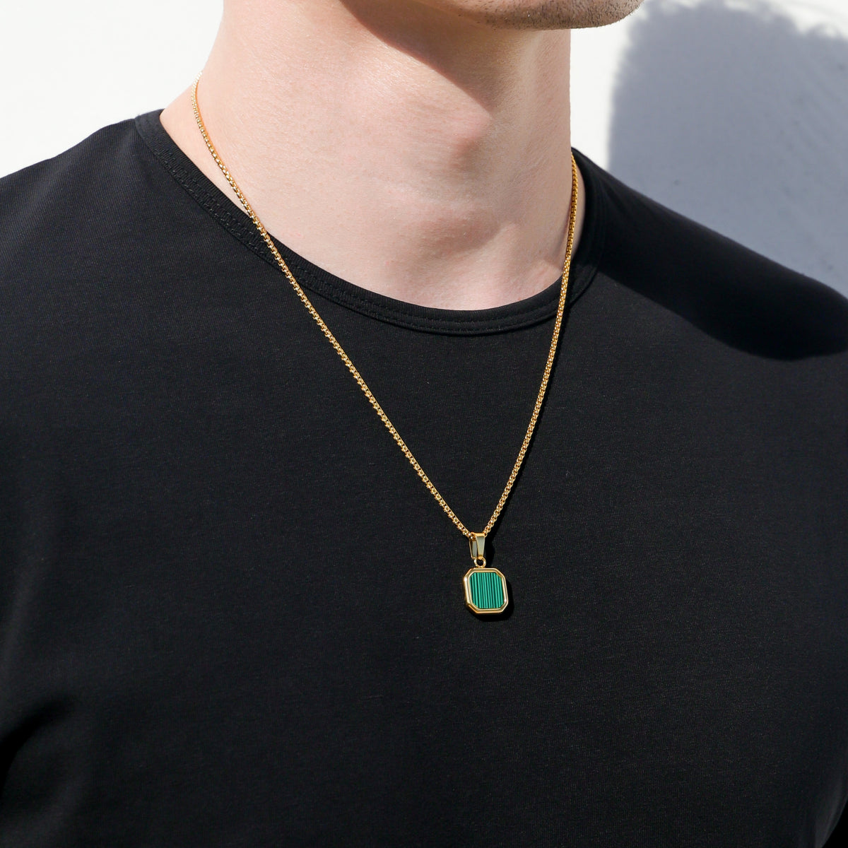 Gold chain necklace with green square pendant centered on black shirt