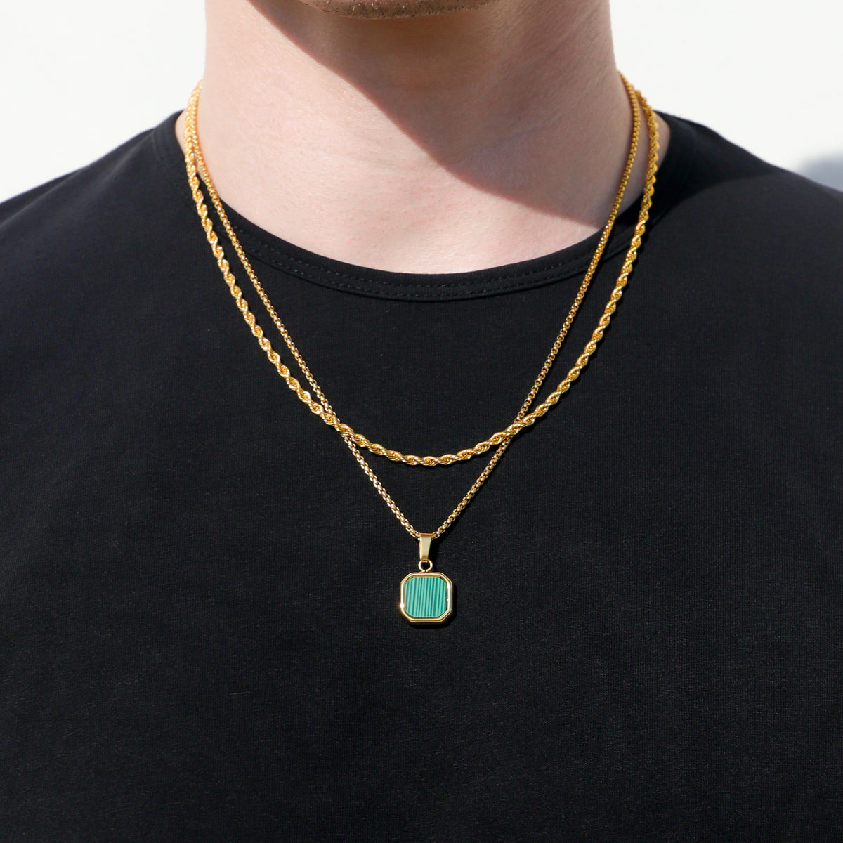 Gold chain necklace with green square pendant on black crewneck shirt