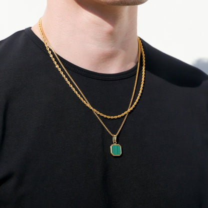 Gold chain necklace with green square pendant on black shirt, angled view