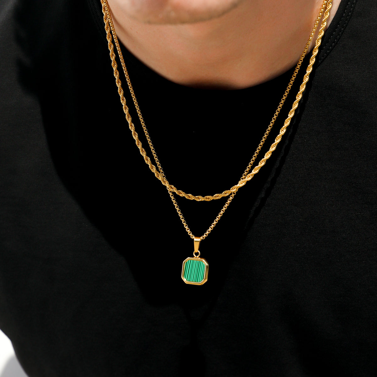 Gold chain necklace with green square pendant charm, close-up on black shirt