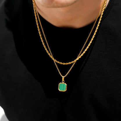 Gold chain necklace with green square pendant charm, close-up on black shirt