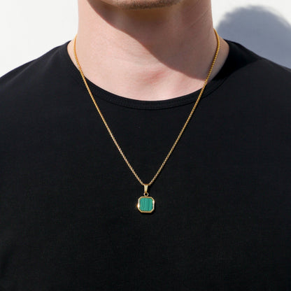 Gold chain necklace with small green square pendant on black crewneck shirt